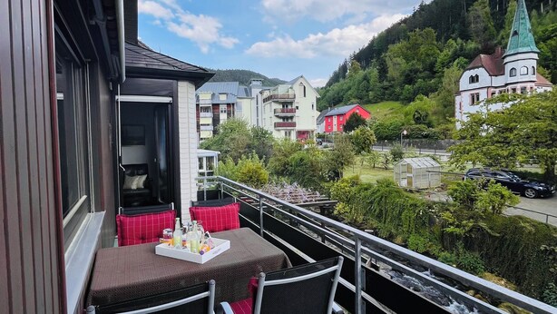 Un balcon avec une table dressée pour deux personnes, donnant sur une rivière et une ville avec ses bâtiments et son église.