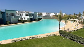 A pool with a clear blue water, surrounded by a well-maintained lawn and a row of white buildings with balconies.