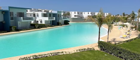 A pool with a clear blue water, surrounded by a well-maintained lawn and a row of white buildings with balconies.
