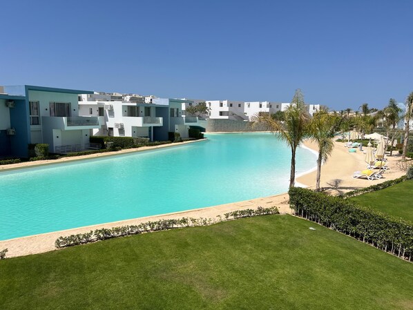 A pool with a clear blue water, surrounded by a well-maintained lawn and a row of white buildings with balconies.