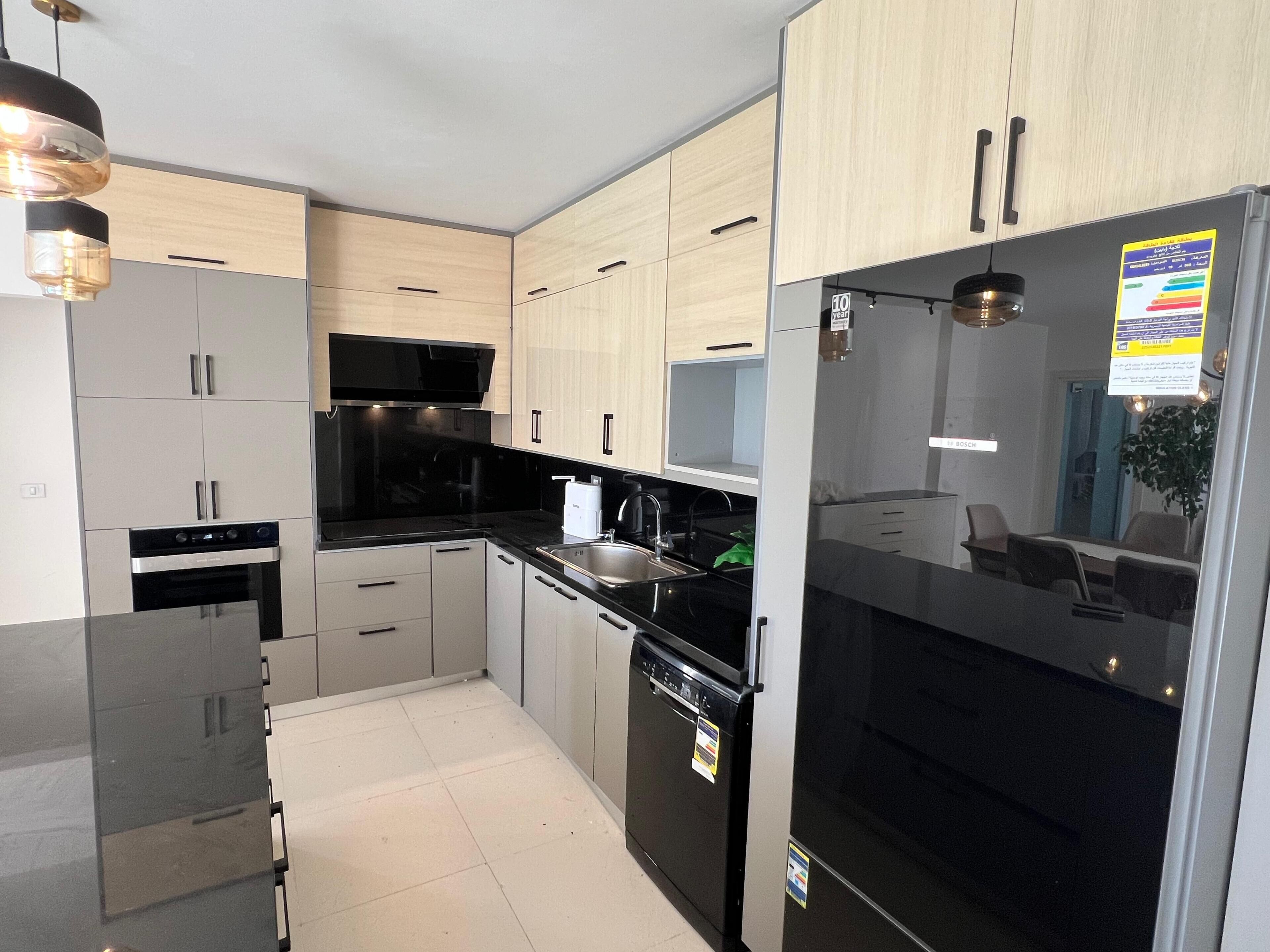 A modern kitchen with black appliances, light wood cabinets, and a Bosch refrigerator.