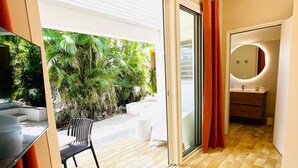 A modern hotel room with a sliding glass door to a patio, a round mirror, a small table with a vase and remote control, and a checkered floor. - Studio Ti'Bwa - Terrace 2 pers, 3mn from Anse Mitan beach (Les Trois-Îlets)