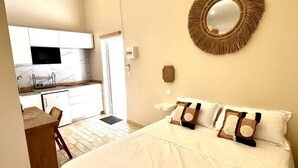 A bedroom with a large bed, a round mirror, and a kitchenette in the background. - Studio Ti'Bwa - Terrace 2 pers, 3mn from Anse Mitan beach (Les Trois-Îlets)
