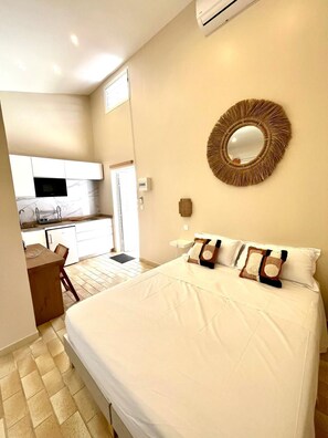 A bedroom with a large bed, a round mirror, and a kitchenette in the background. - Studio Ti'Bwa - Terrace 2 pers, 3mn from Anse Mitan beach (Les Trois-Îlets)