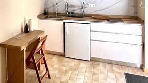 A compact kitchen with white cabinets, a microwave, a small refrigerator, and a wooden table with a chair. - Studio Ti'Bwa - Terrace 2 pers, 3mn from Anse Mitan beach (Les Trois-Îlets)