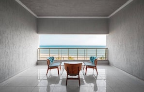A room with a view of the sea, a balcony with a railing, and a table with chairs.
