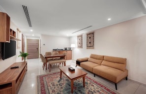 Una sala de estar con sofá, televisión, muebles de madera, un comedor y una cocina al fondo.