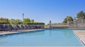 A swimming pool with a stone wall and a metal fence. - Enjoy Labor Day weekend in a beautiful 2 BR fully equipped luxury suite. (Boyne Falls)