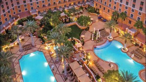 Et hotel med flere swimmingpools, palmer og udendørs siddeområder.