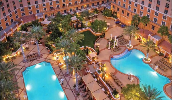 Un hotel con diverse piscine, palme e aree salotto all'aperto.