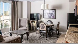 Et hotelværelse med ventilator, spisebord med stole, fjernsyn og et vindue med gardiner.