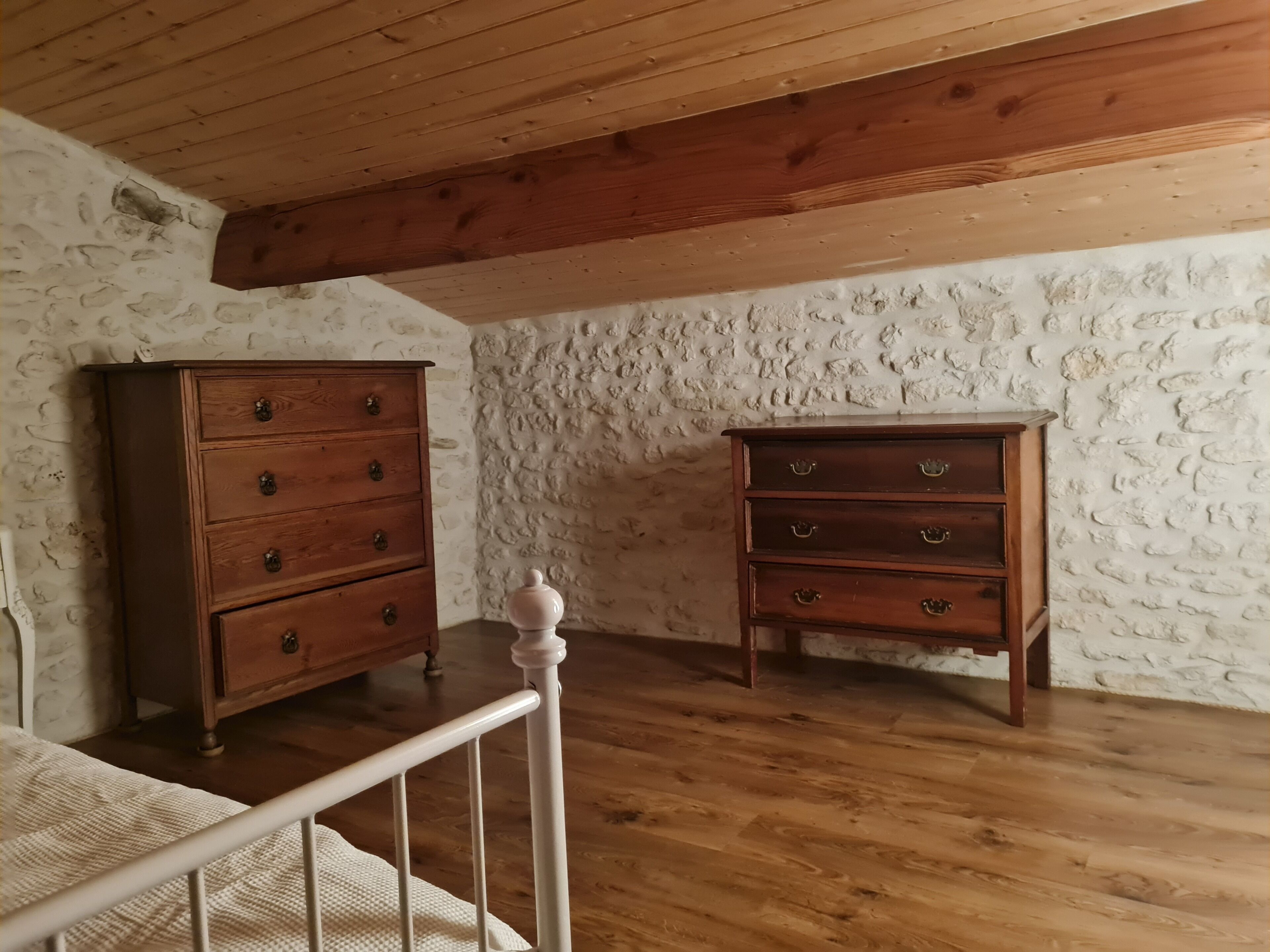 Een kamer met houten vloeren, een wit bed en twee houten kasten tegen een wand met textuur.