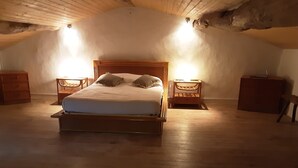 Ett sovrum med en säng i trä, två sängbord och ett sluttande tak.
