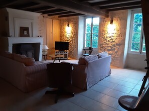 Un salon avec une cheminée, un téléviseur, un mur en pierre et de grandes fenêtres.
