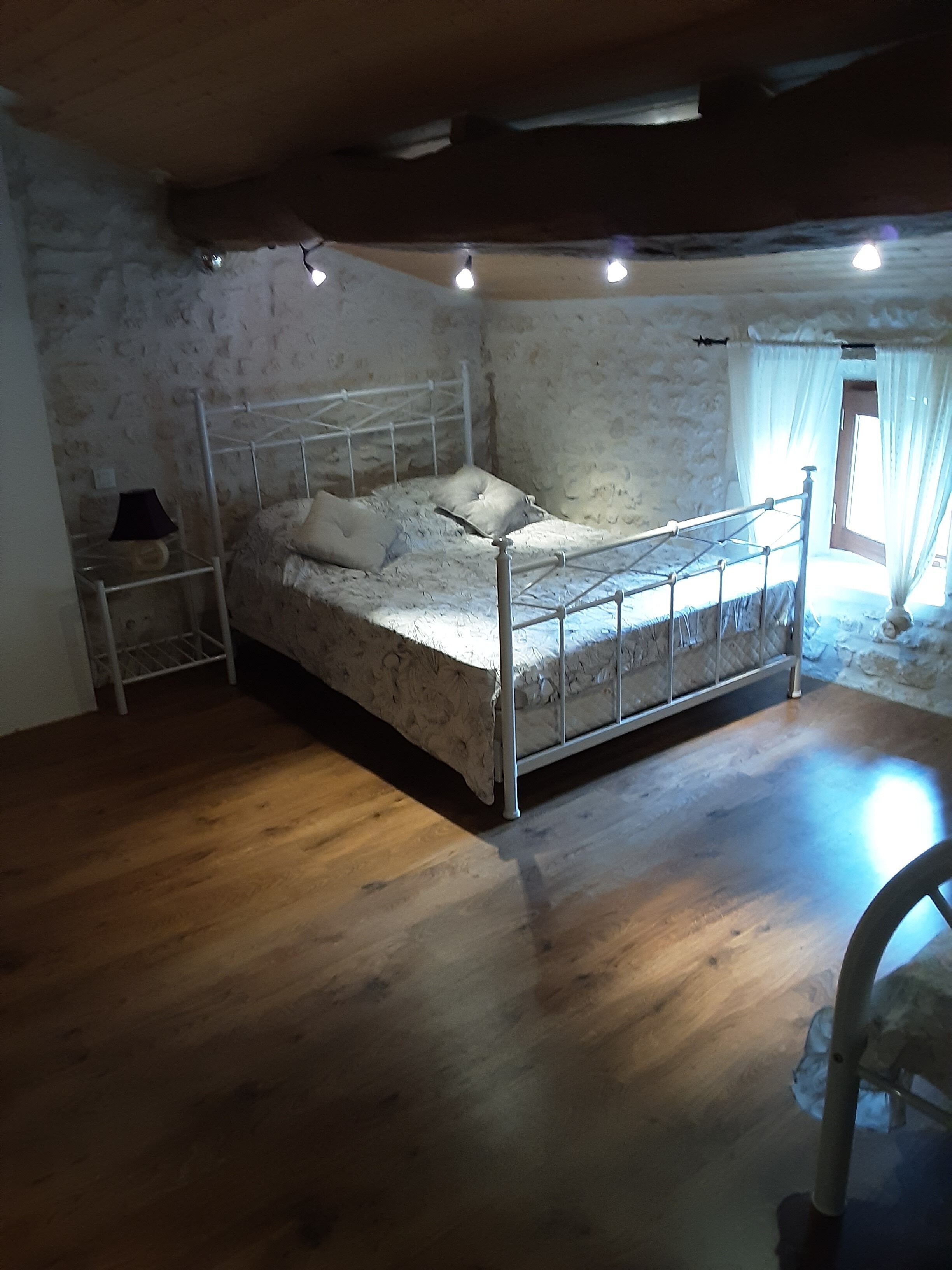 A bedroom with a metal bed frame, a wooden floor, and a stone wall.