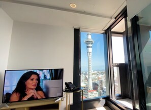 A modern hotel room with a large TV, a small table with a phone, and a view of a cityscape and a tower. - Amazing Skytower & Sea View 2BR/2BA Apartment (Auckland)