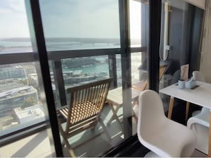 Un balcon donnant sur une marina et des immeubles, une chaise en bois et une petite table avec une tasse et une cuillère.
