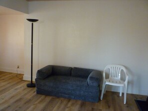 Uma sala de estar com um sofá cinza escuro, uma cadeira de plástico branca e um abajur de chão alto.