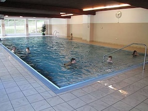 Ein Hallenbad mit gefliesten Böden und Wänden, einer Uhr an der Wand und einigen schwimmenden Personen.