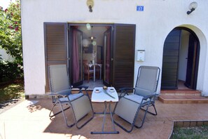 Eine Terrasse im Freien mit zwei Stühlen, einem Tisch, einer Tür mit Hinweisschild und einem kleinen Tisch mit einer Flasche und Gläsern.
