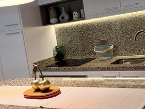 Una cocina con encimeras de granito, un lavabo, una planta y un frutero decorativo para manzanas.