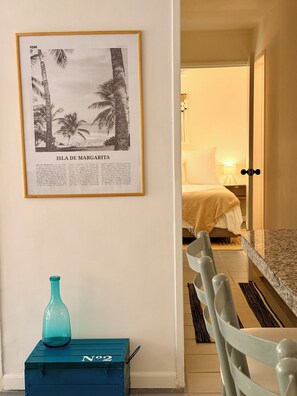 Un cuadro con la Isla de Margarita, un caja azul para guardar cosas y una zona de comedor con una silla.