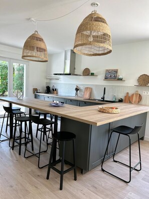 Et moderne køkken med en central ø, sorte barstole og to kurvependler.