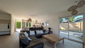 A modern living room with a black leather sofa, wooden coffee table, and a kitchen in the background. - Villa Oïhana 4*, 5 suites, Heated pool, Beach 5 km (Labenne)