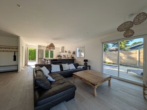 A modern living room with a black leather sofa, wooden coffee table, and a kitchen in the background. - Villa Oïhana 4*, 5 suites, Heated pool, Beach 5 km (Labenne)