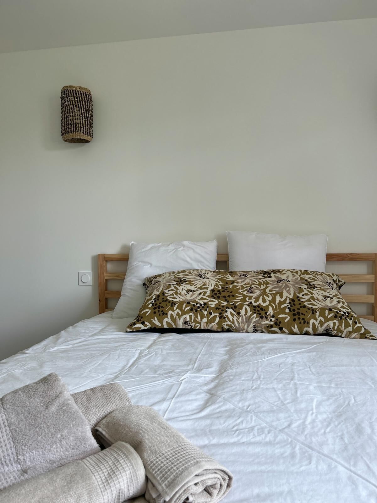 A bed with white bedding, a patterned pillow, and a rolled towel on the floor.