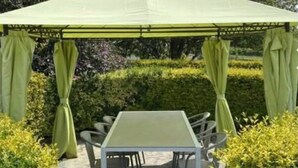 Un kiosque abrité, avec une table et des chaises, entouré de haies et d’arbres.