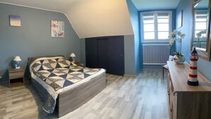 Une chambre à coucher comprenant un lit, des tables de chevet, une commode, une fenêtre avec des stores et un radiateur.