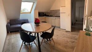 Un espace de vie compact comprenant un coin repas, une kitchenette et un canapé gris.