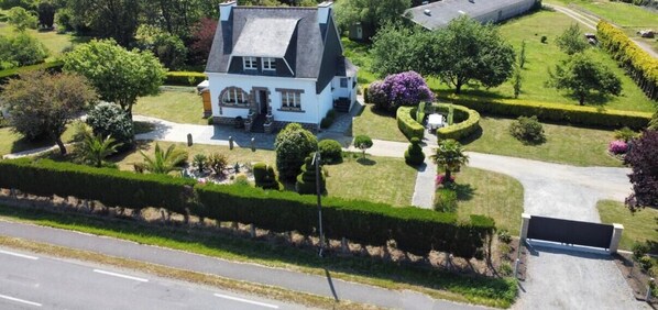A large house with a steep roof, surrounded by well-manicured gardens and a paved driveway. - The camellia house (Trégunc)