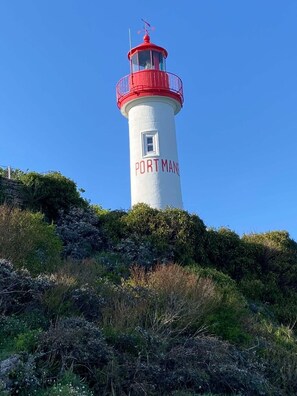 A lighthouse with 'PORT MAN' written on its side, surrounded by vegetation. - The camellia house (Trégunc)
