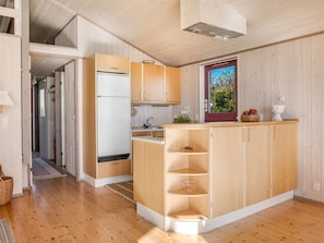 A compact kitchen with wooden cabinets, a built-in refrigerator, and a small island with shelves. - "Stefan" - 50m from the sea by Interhome (Odder)