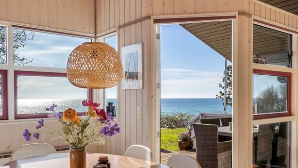 A wooden interior with a round table, a wicker chair, a wicker sofa, a wicker lamp, and a view of the sea. - "Stefan" - 50m from the sea by Interhome (Odder)