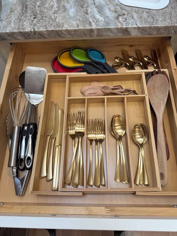 A drawer with kitchen utensils including spatulas, whisks, knives, forks, and spoons.