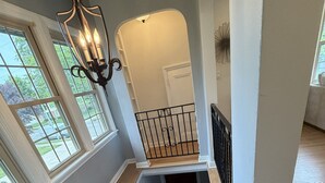 A staircase with wooden steps and a black railing, leading to a landing with a white wall and a decorative light fixture. - Walk to the Waves and the Zoo Main St (Racine)