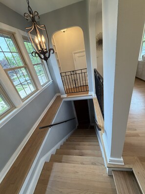 A staircase with wooden steps and a black railing, leading to a landing with a white wall and a decorative light fixture. - Walk to the Waves and the Zoo Main St (Racine)