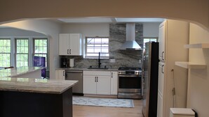 A modern kitchen with white cabinets, a marble countertop, a built-in stove, and a large window. - Walk to the Waves and the Zoo Main St (Racine)
