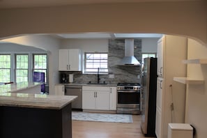 A modern kitchen with white cabinets, a marble countertop, a built-in stove, and a large window. - Walk to the Waves and the Zoo Main St (Racine)
