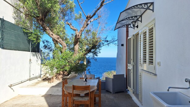 Eine Terrasse mit Tisch und Stühlen, Blick aufs Meer und ein Gebäude mit Fensterläden.
