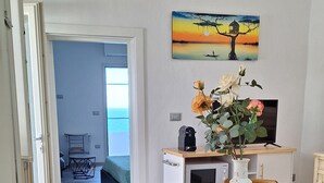Ein Essbereich mit einem runden Tisch, Stühlen, einer Blumenvase, einem Bild an der Wand und einer kleinen Küchenzeile im Hintergrund.