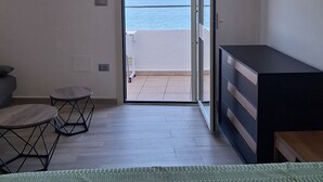 Ein Schlafzimmer mit Bett, Schreibtisch und Meerblick durch eine offene Tür.