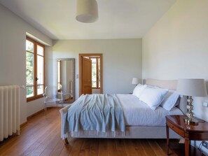 Ein Schlafzimmer mit einem Bett, einem Nachttisch, einer Lampe und einem großen Fenster.
