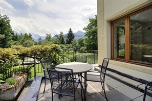 Eine Terrasse mit rundem Tisch und Stühlen, Blick auf Berge und ein Garten mit Zaun.