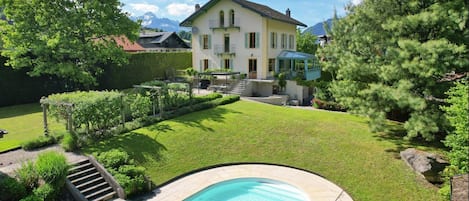 A house with a swimming pool, surrounded by a well-maintained lawn and trees.