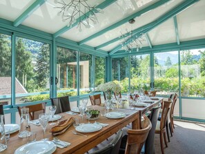 A conservatory with a dining table set for a meal, surrounded by large windows offering a view of a lush garden and distant mountains. - Chalet Nivicare for 14 pax
Walking distance to ski gondola and village center (Saint-Gervais-les-Bains)