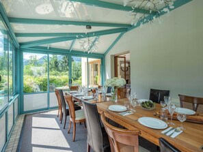 Ein Essbereich mit einem Tisch für sechs Personen, großen Fenstern und Blick auf Grünflächen.